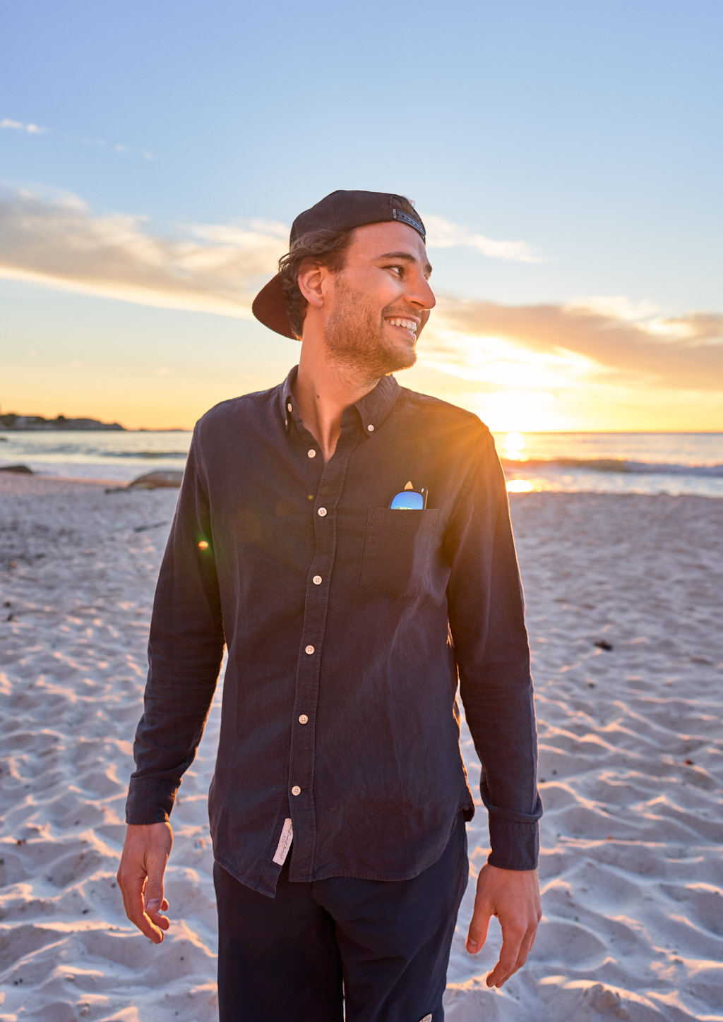 Smiling young man standing infront of the sunset at the beach.