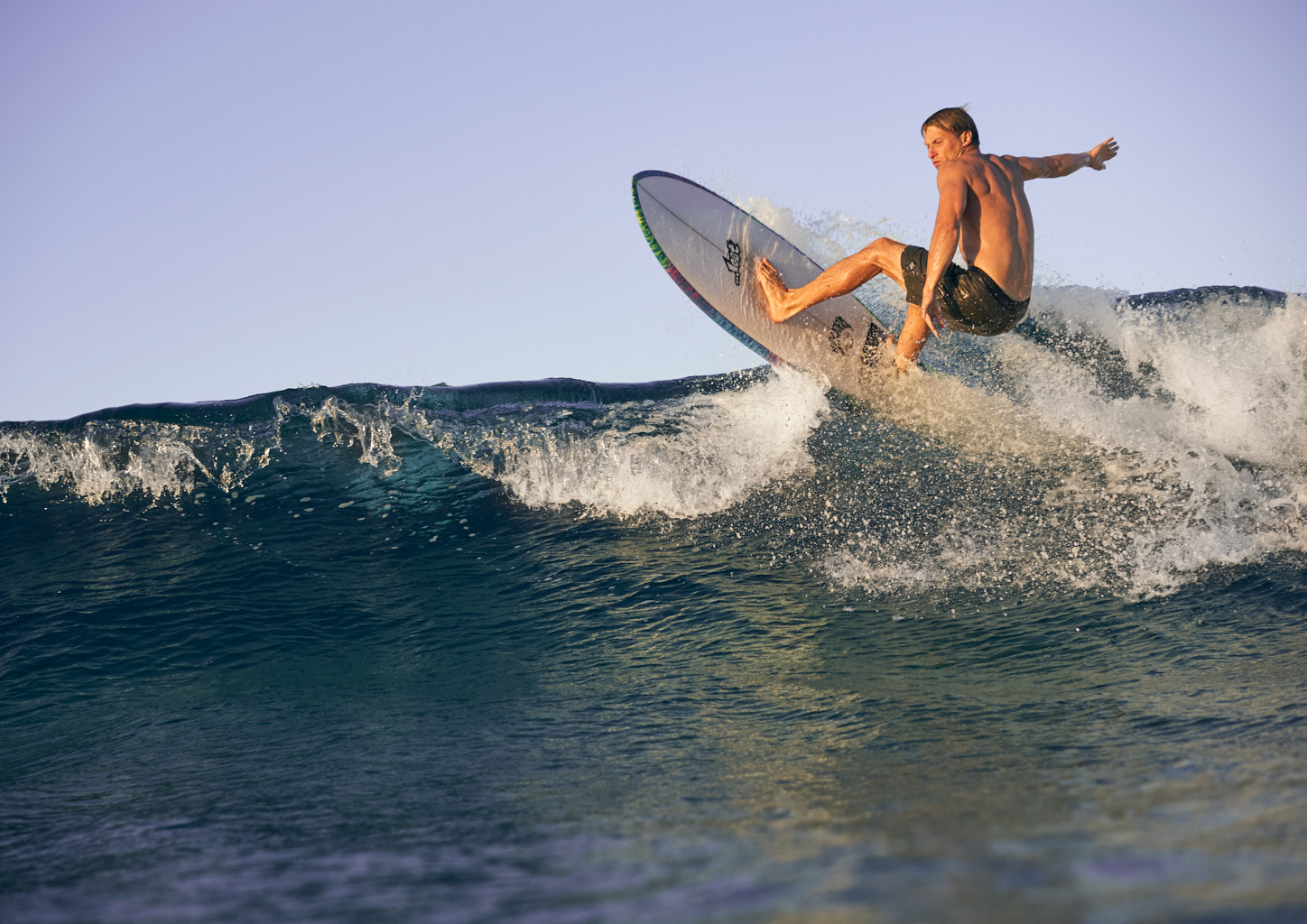 Male surfer performing a frontside turn on the lip of the wave.